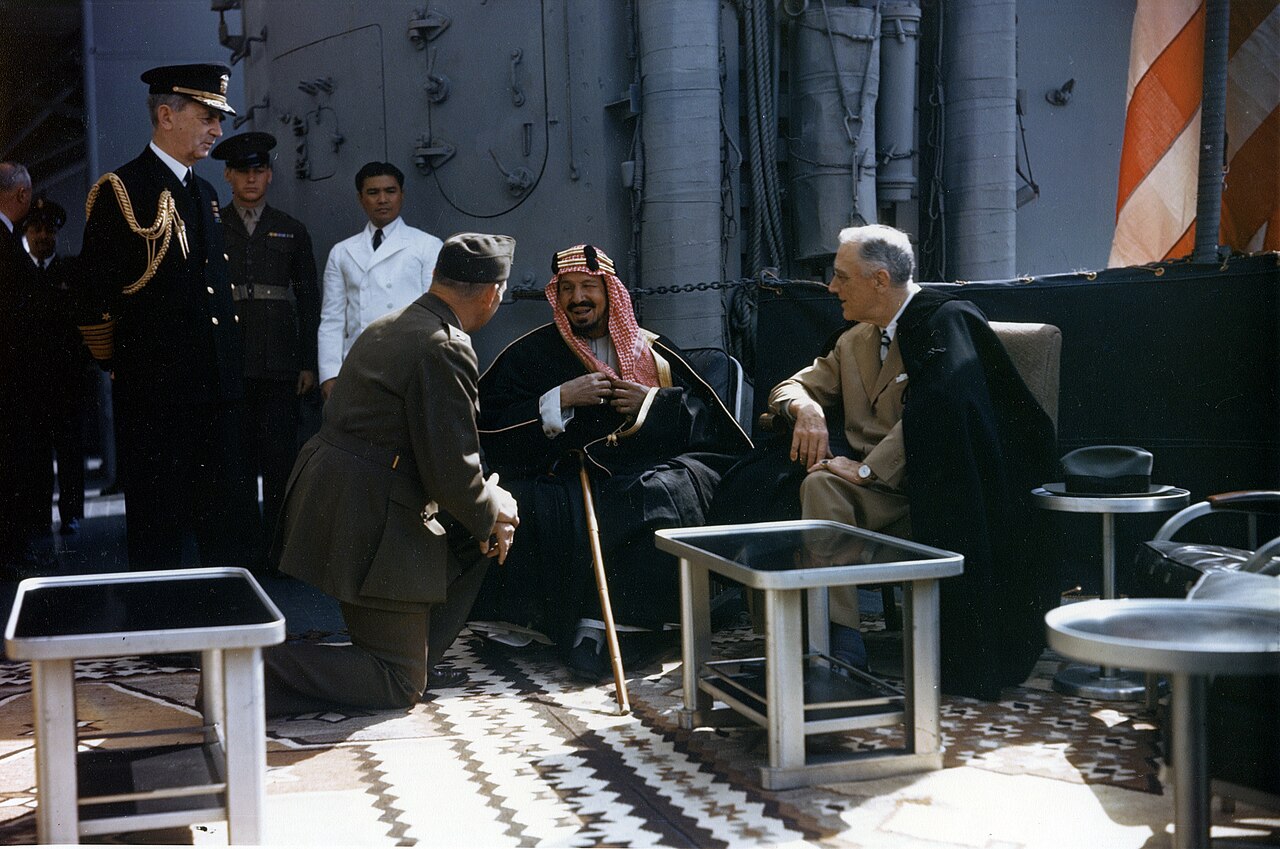 King Ibn Saud, seated at center, and Franklin Roosevelt, seated at right, meet aboard USS Quincy with interpreter William Eddy between them.